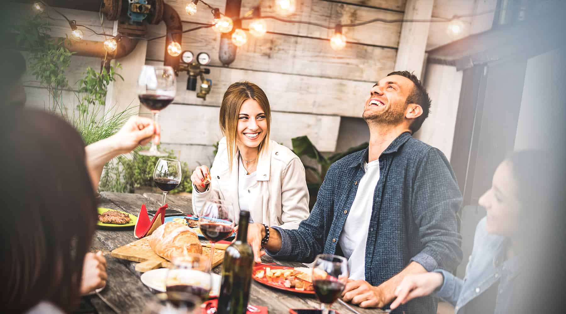 Man and woman enjoying dinner and wine with a group of friends under string lights