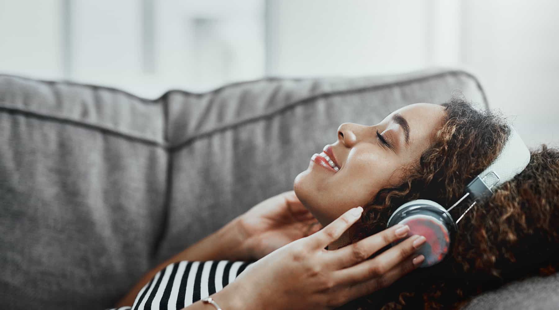 Woman in a striped t-shirt laying on a couch with over the ear headphones