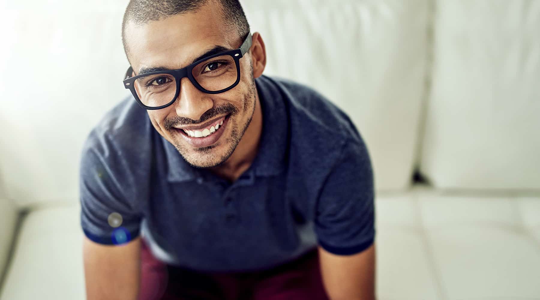 Young man in a blue collard shirt wearing glasses and smiling