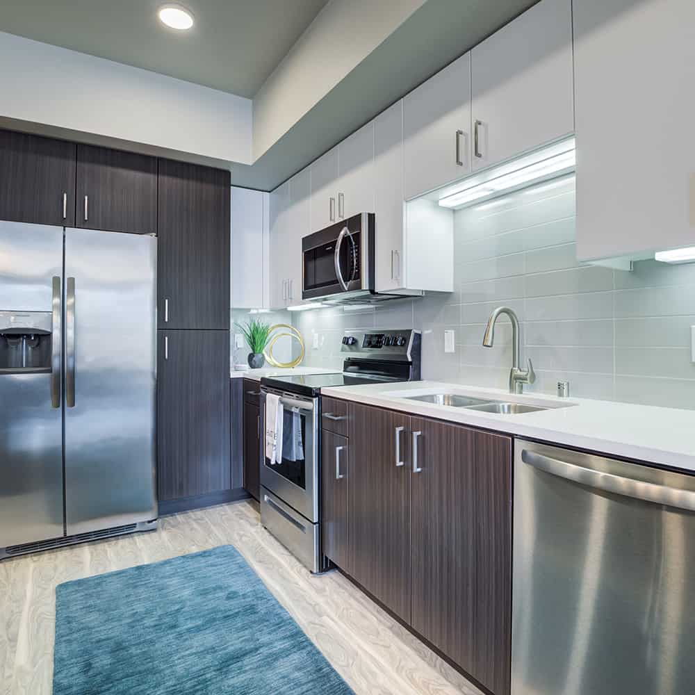 Modern and spacious kitchen featuring wood style flooring, stainless steel appliances and white cabinets.