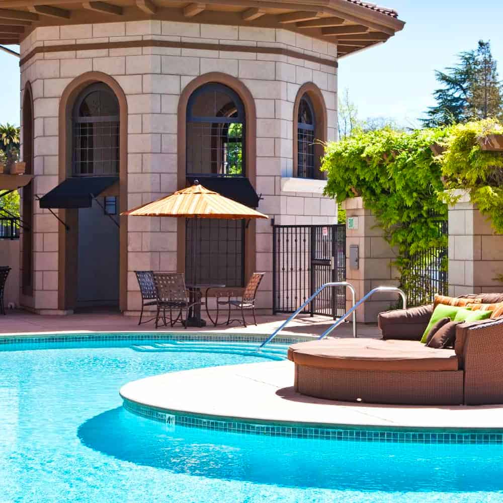 An outdoor swimming pool, with a cushioned couch nearby on a sunny day in Concorde, CA